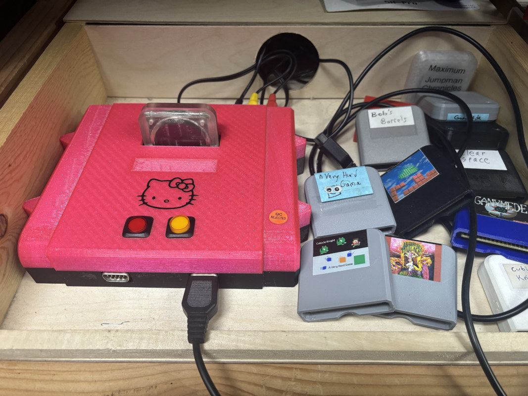 The famous Hello Kitty edition GameTank, at its home of HackManhattan. To its side are a number of GameTank cartriges, including the final AVHG cartridge and one from earlier in development